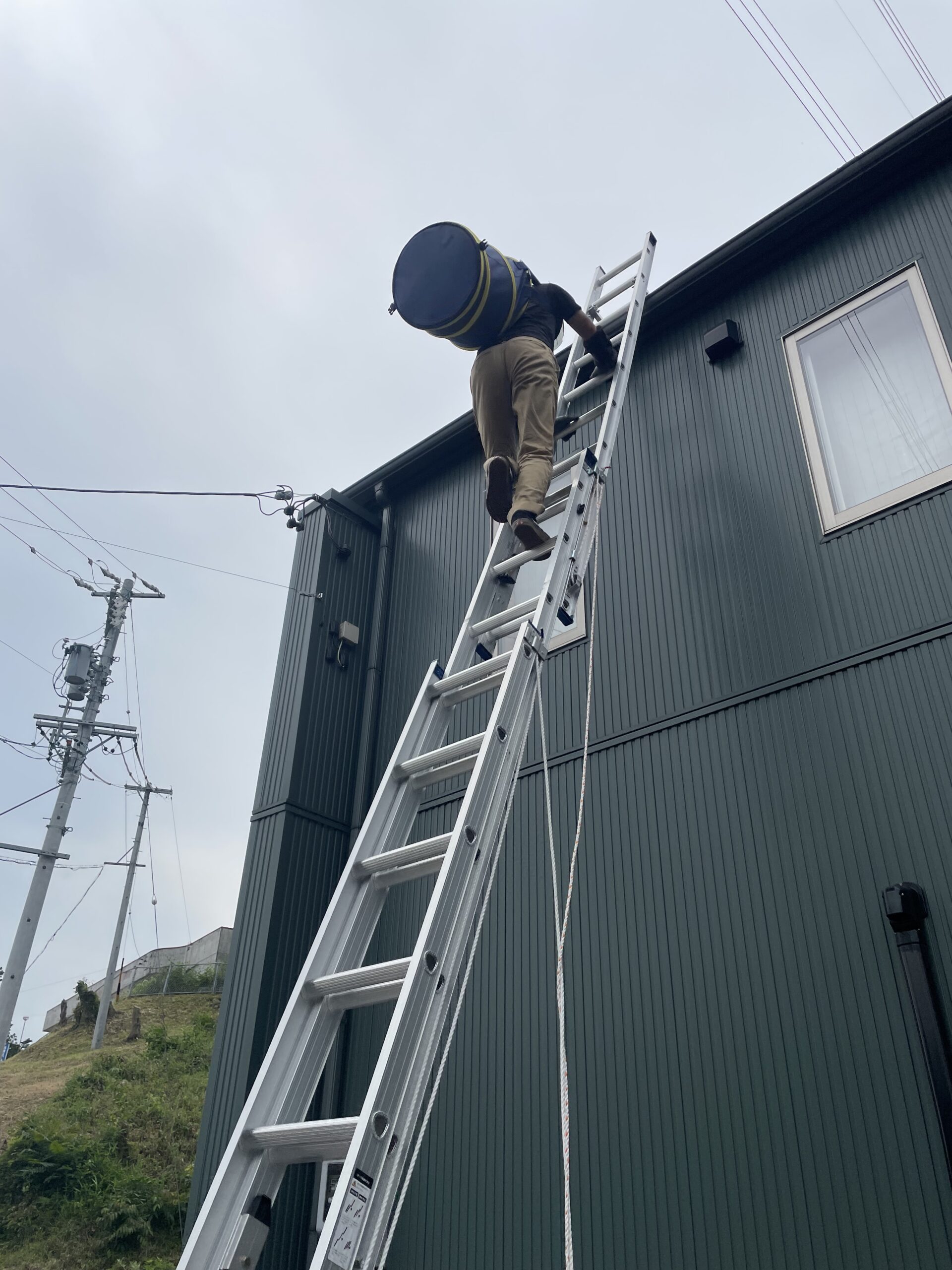 はしごで屋根に上がり煙突掃除をする